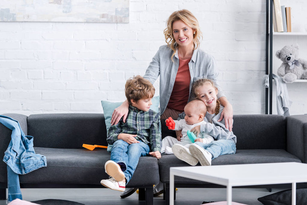 happy mother smiling at camera while spending time with three adorable little kids at home  - Foto, Bild