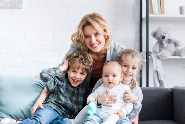 schöne glückliche Mutter mit drei entzückenden Kindern, die in die Kamera lächeln  - Foto, Bild