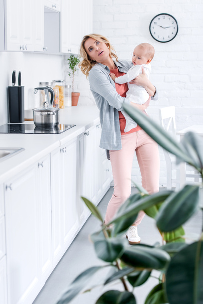 exhausted mother holding adorable infant child while cooking in kitchen - Fotoğraf, Görsel