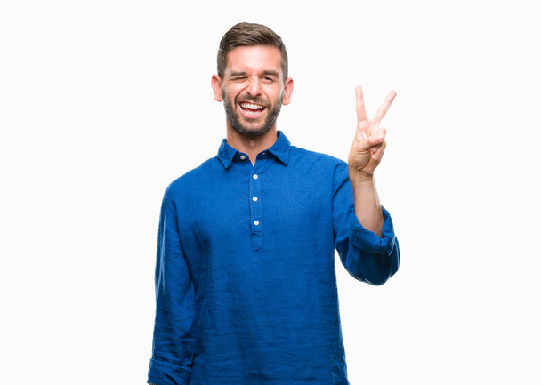 Young handsome man over isolated background smiling with happy face winking at the camera doing victory sign. Number two. - Photo, Image