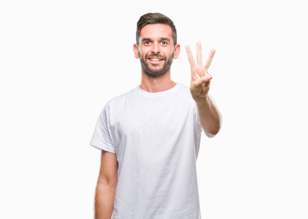 Jonge knappe man over geïsoleerde achtergrond weergeven en met de vingers omhoog nummer drie terwijl lacht zelfverzekerd en blij. - Foto, afbeelding