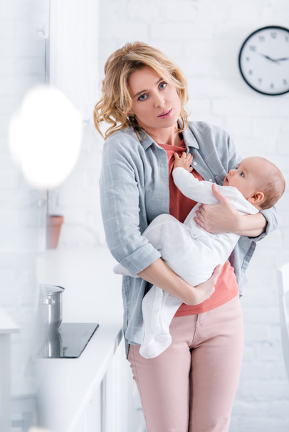 exhausted mother holding adorable infant child and looking at camera - Foto, imagen