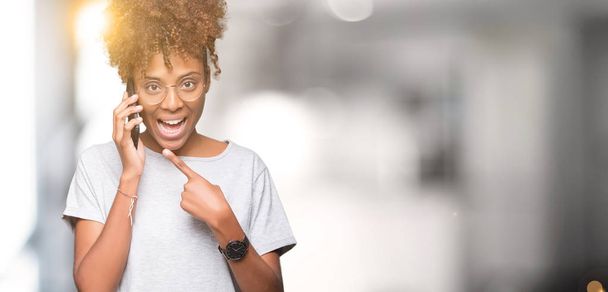 Nuori afrikkalainen amerikkalainen nainen puhuu älypuhelimella eristetyn taustan yli erittäin onnellinen osoittaen kädellä ja sormella
 - Valokuva, kuva
