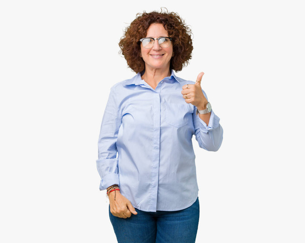 Piękny środkowy ager senior Business kobietę w okularach na białym tle robi szczęśliwy kciuk w górę gest ręką. Zatwierdzająca wyrażenie patrząc na kamery, pokazujące sukces. - Zdjęcie, obraz