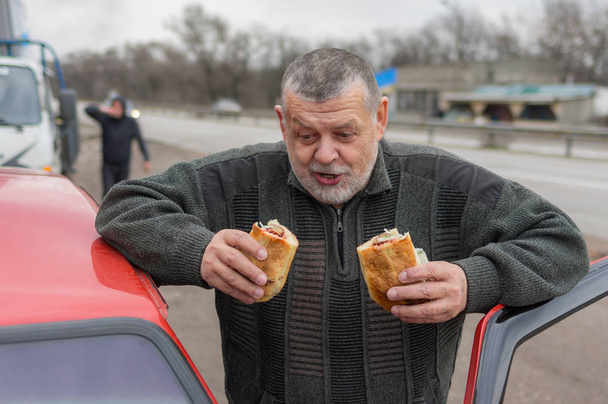 Portrait of Caucasian hungry senior driver ready to eat street food near his car - Photo, Image