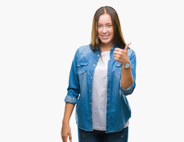 Young caucasian beautiful woman over isolated background doing happy thumbs up gesture with hand. Approving expression looking at the camera with showing success. - Фото, зображення