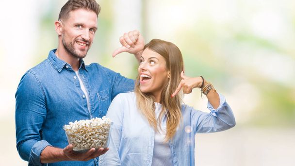Giovane coppia innamorata mangiare popcorn su sfondo isolato con faccia a sorpresa puntando il dito verso se stesso
 - Foto, immagini