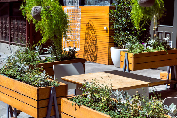 Café d'été avec une table brune en bois et des pots de fleurs en bois avec des plantes, un endroit vide dans le restaurant
. - Photo, image