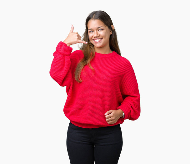 Joven mujer morena hermosa vistiendo suéter rojo de invierno sobre fondo aislado sonriendo haciendo gesto de teléfono con la mano y los dedos como hablando por teléfono. Comunicar conceptos
. - Foto, Imagen