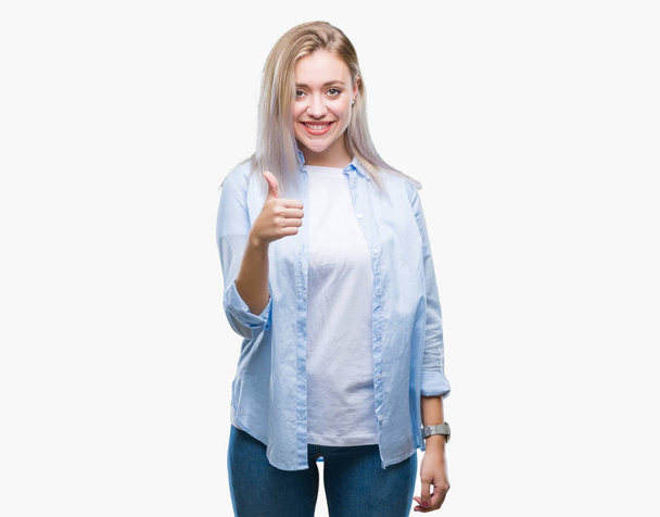 Young blonde woman over isolated background doing happy thumbs up gesture with hand. Approving expression looking at the camera with showing success. - Foto, imagen
