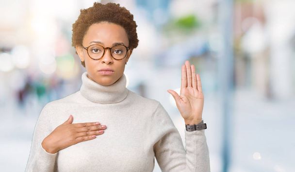 Jovem mulher afro-americana bonita vestindo óculos sobre fundo isolado Jurando com a mão no peito e palma aberta, fazendo uma promessa de lealdade juramento
 - Foto, Imagem