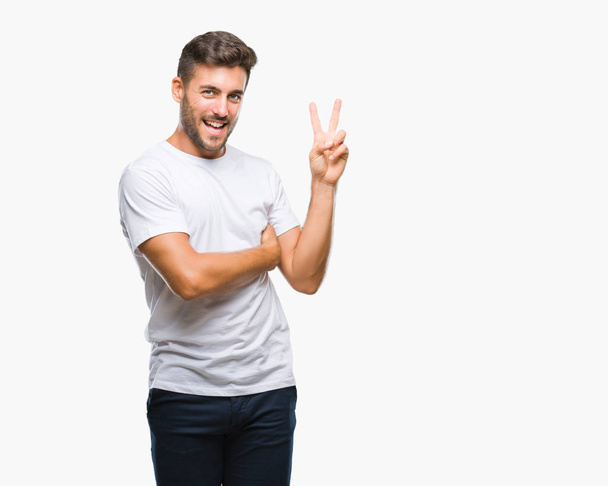 Young handsome man over isolated background smiling with happy face winking at the camera doing victory sign. Number two. - Photo, Image