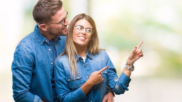 Jeune couple amoureux portant des lunettes sur fond isolé souriant et regardant la caméra pointant avec deux mains et doigts sur le côté
. - Photo, image