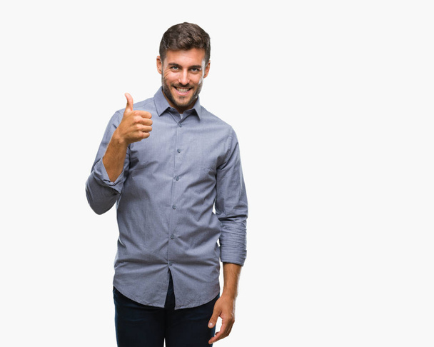 Young handsome man over isolated background doing happy thumbs up gesture with hand. Approving expression looking at the camera with showing success. - Photo, image