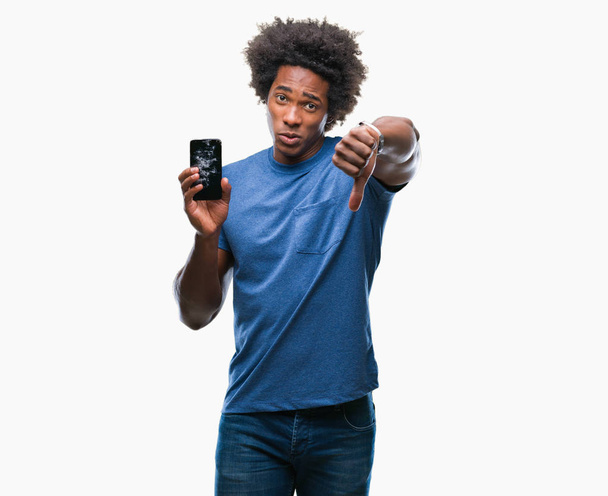 Афро американський людина тримає сломанной смартфон за ізольованих фону з сердитися обличчя, ознака від'ємного числа показує неприязнь з великі пальці вниз, відмова концепції - Фото, зображення