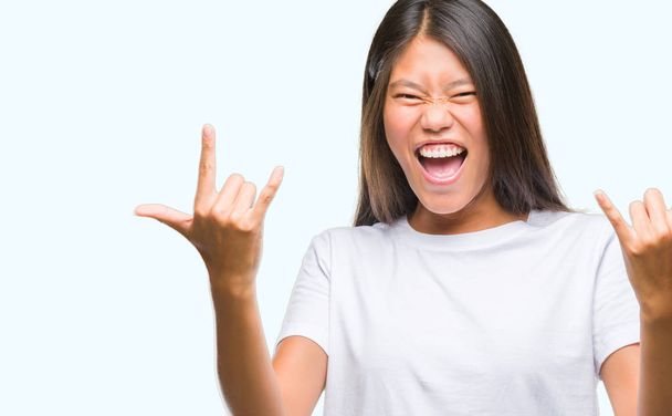 Mujer asiática joven sobre fondo aislado gritando con expresión loca haciendo símbolo de roca con las manos arriba. Estrella de la música. Concepto pesado
. - Foto, Imagen