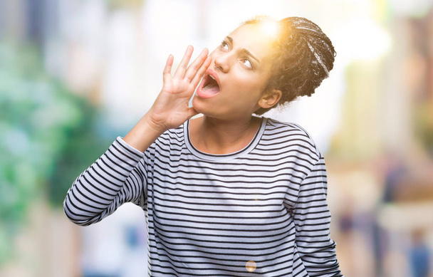 Genç örgülü saç Afro-Amerikan Kız bağırarak ve ağzı üzerinde el ile yan için çığlık izole arka plan üzerinde kazak giyiyor. İletişim kavramı. - Fotoğraf, Görsel