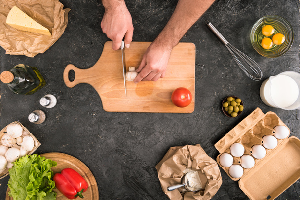cropped view of man chopping mushroom on cutting board with pizza ingredients on grey background  - Photo, Image