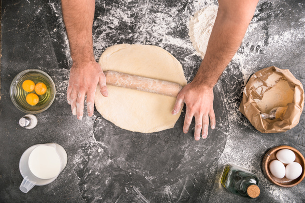 cropped view of man rolling pizza dough with wooden pin on grey background - Foto, afbeelding