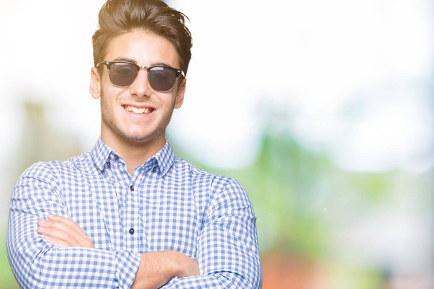 Young handsome man wearing sunglasses over isolated background happy face smiling with crossed arms looking at the camera. Positive person. - Fotó, kép