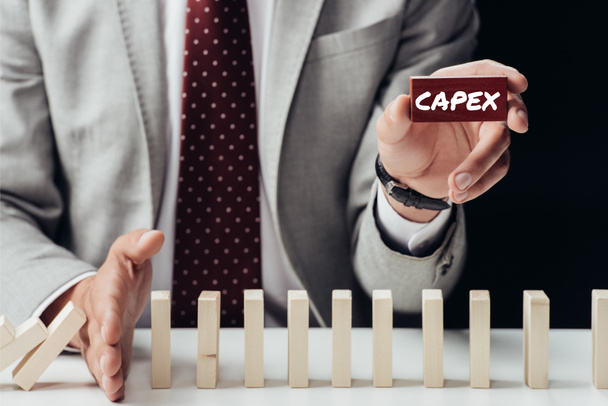 gedeeltelijke weergave van zakenman baksteen met 'capex' woord te houden en het voorkomen van houten blokken vallen - Foto, afbeelding