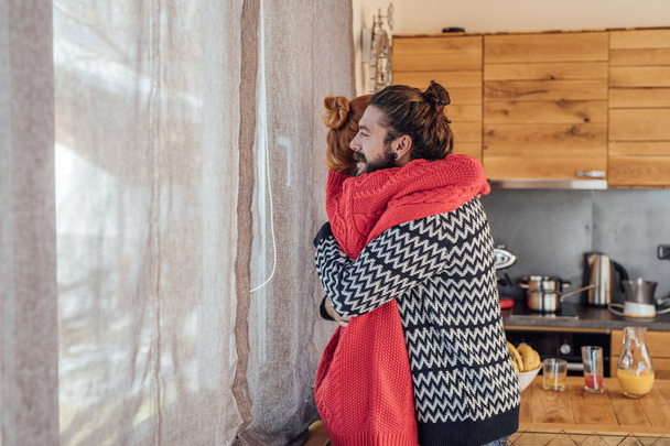 Happy man and woman hugging and enjoying wintertime at home. - Φωτογραφία, εικόνα