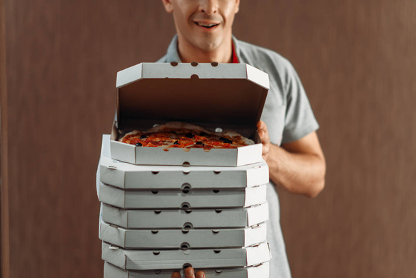 Delivery man shows fresh pizza in box, delivering service. Courier from pizzeria holds cardboard packages indoors - Fotó, kép