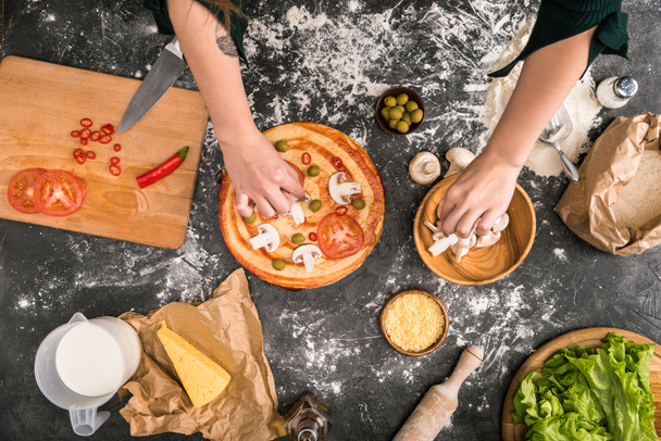 Μερική άποψη της γυναίκας βάζοντας υλικά στην πίτσα σε γκρι φόντο με αλεύρι  - Φωτογραφία, εικόνα