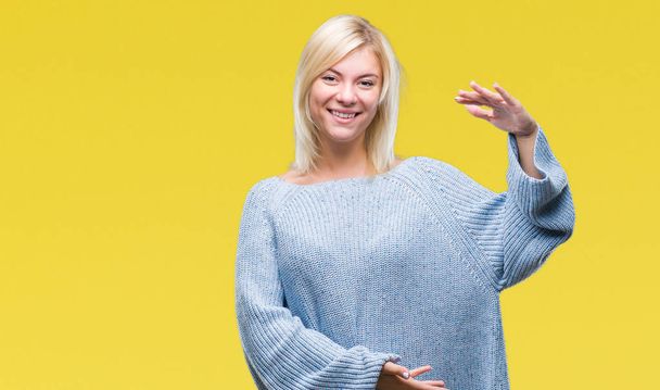 Young beautiful blonde woman wearing winter sweater over isolated background gesturing with hands showing big and large size sign, measure symbol. Smiling looking at the camera. Measuring concept. - Photo, Image