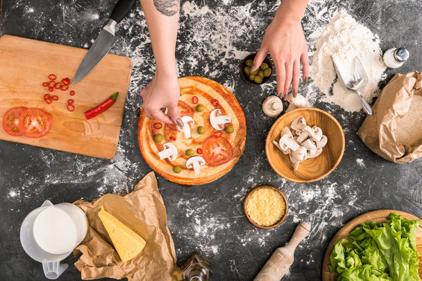 vista recortada de la mujer poniendo ingredientes en la pizza sobre fondo gris con harina
  - Foto, Imagen