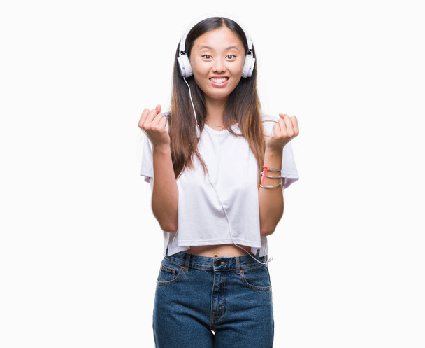 Nuori aasialainen nainen kuuntelee musiikkia yllään kuulokkeet eristetty tausta huutaa ylpeä ja juhlii voittoa ja menestystä hyvin innoissaan, hurraavat tunteet
 - Valokuva, kuva