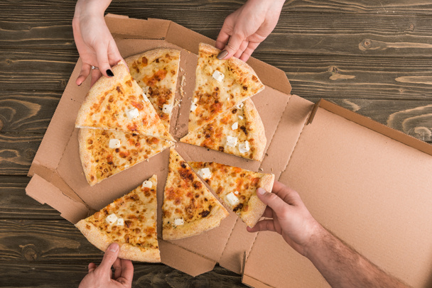 vue recadrée d'amis mangeant de la pizza au fromage sur une table en bois
 - Photo, image