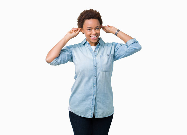 junge schöne afrikanisch-amerikanische Frau über isoliertem Hintergrund lächelnd, die Ohren mit den Fingern zuziehend, lustige Geste. Vorsprechen-Problem - Foto, Bild