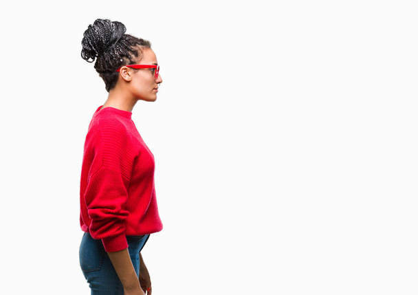 Jonge gevlochten hair Afrikaans Amerikaans meisje trui en bril dragen over geïsoleerde achtergrond op zoek naar kant, ontspannen profiel pose met natuurlijke gezicht met vertrouwen glimlach. - Foto, afbeelding