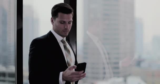 Businessman using smartphone in skyscraper office - Filmati, video