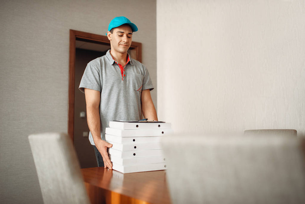 Chłopiec dostawy pizzy pozostawia zamówienia na stole, dostarczanie usługi. Kurier z pizzeria posiada kartonowe opakowania wewnątrz - Zdjęcie, obraz
