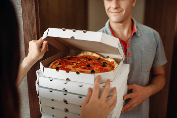Delivery man shows fresh and hot pizza to female customer at the door, delivering service. Deliver from pizzeria and woman near the entrance to the apartment, pizzaman and buyer - Foto, immagini