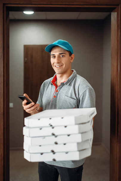 Repartidor de pizza en camiseta y gorra llama al cliente, entregando servicio. Mensajero de pizzería sostiene paquetes de cartón y teléfono
 - Foto, imagen