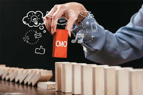 cropped view of woman picking red block with word 'cmo' out of wooden bricks, icons on foreground - Photo, Image