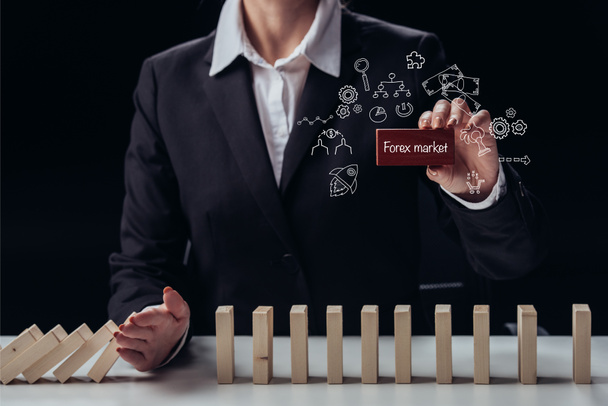 cropped view of businesswoman holding red brick with words 'forex market' while preventing wooden blocks from falling, icons on foreground - Photo, Image