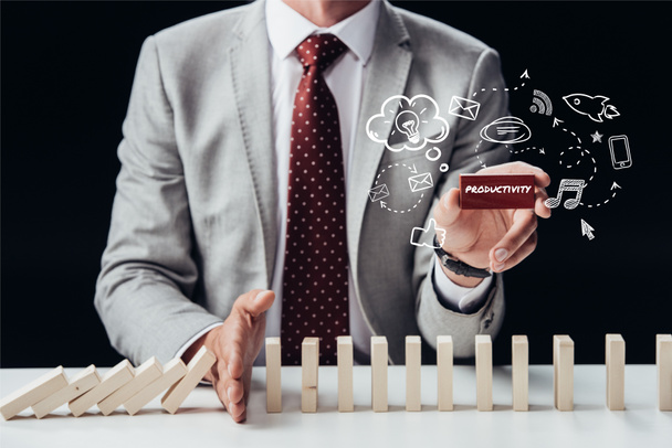 cropped view of businessman preventing wooden blocks from falling while holding brick with word 'productivity', icons on foreground - Фото, изображение