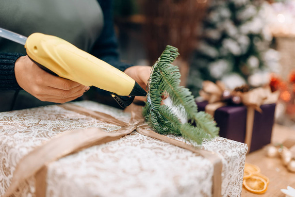 Рождественская упаковка подарков и украшение еловой веткой. Женские обертки на столе, процедура декора, праздничный пакет
 - Фото, изображение