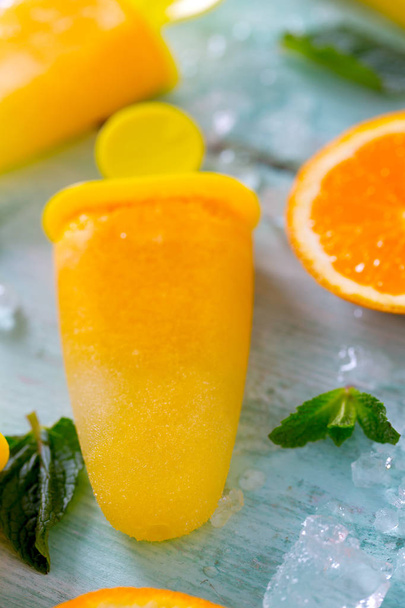 home made orange popsicles on turquoise wooden surface - Fotó, kép