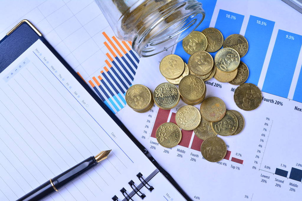 Münzen, die aus dem Glas auf den Business Stock Charts fließen - Geschäftskonzept - Foto, Bild