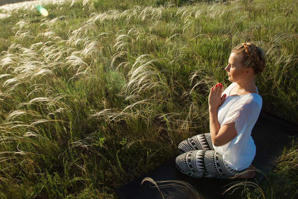 Girl meditates sitting on a beautiful green meadow - Valokuva, kuva