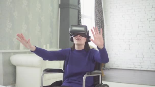 young beautiful disabled woman in a wheelchair at home, uses 3d technology, vr helmet - Кадры, видео