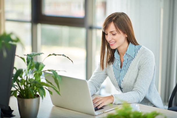 Jonge vrouw werken bij laptop zittend aan tafel in kantoor  - Foto, afbeelding