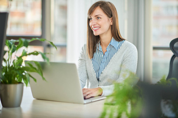Young woman working at laptop while sitting at table in office  - Photo, Image
