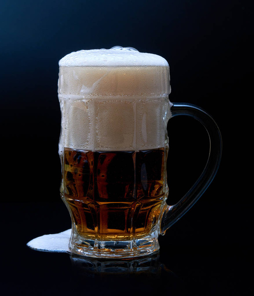 Стеклянная кружка пива с пеной изолированы на темном фоне
. - Фото, изображение