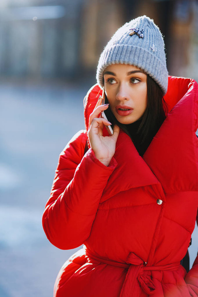 Une fille qui parle sur son portable. Belle fille heureuse en bonnet tricoté gris et manteau d'hiver rouge sur téléphone portable en journée d'hiver. Concept de communication. - Image
. - Photo, image